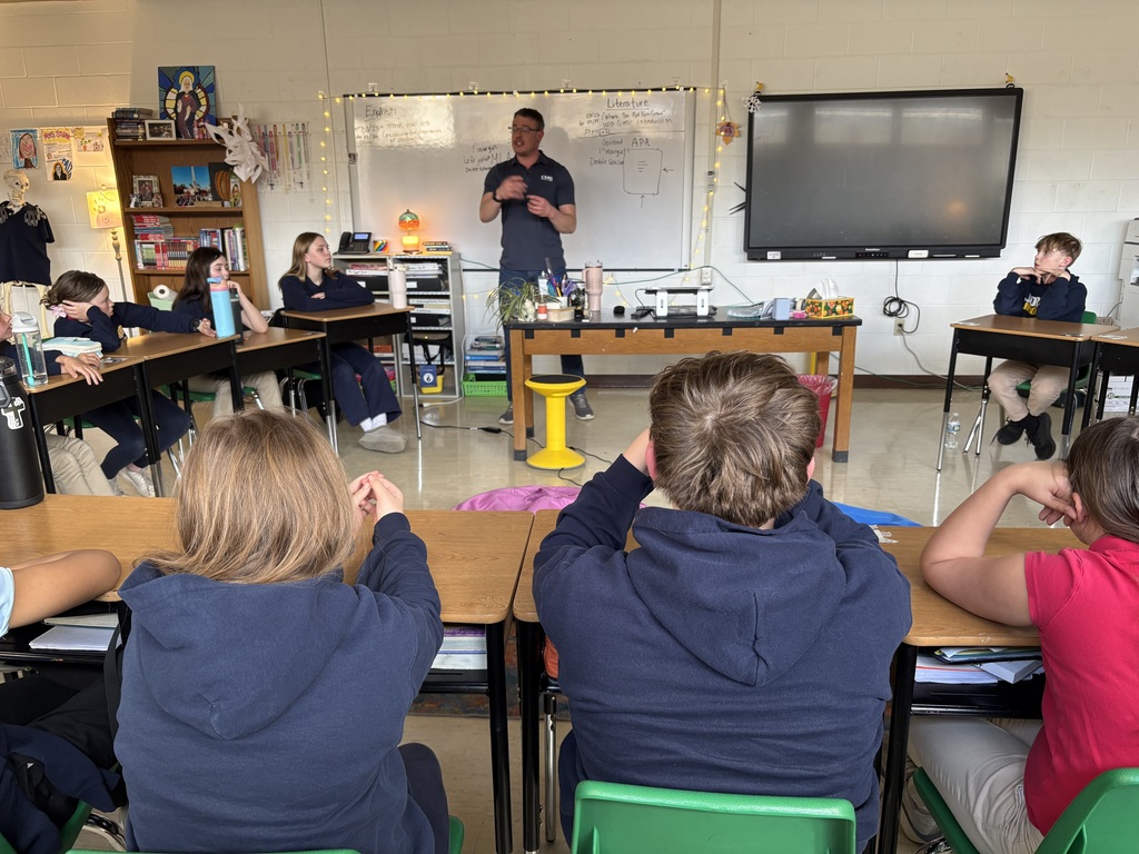 students seated at desks in a classroom listening to a presentation