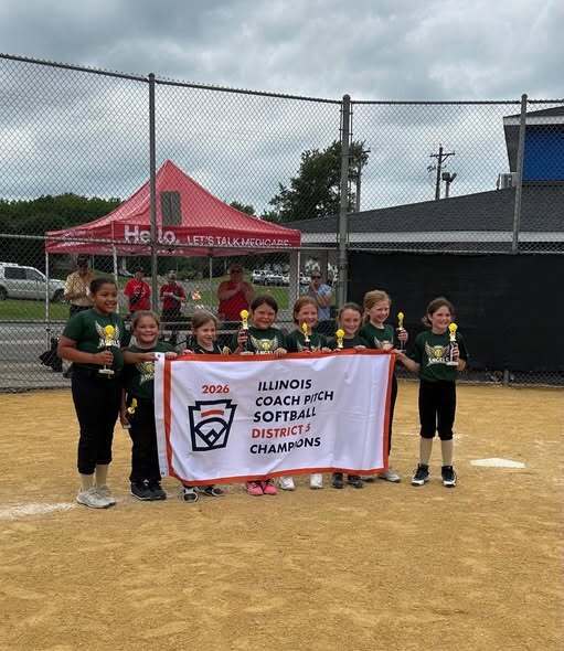 eight softball players posing with their championship banner on a softball field