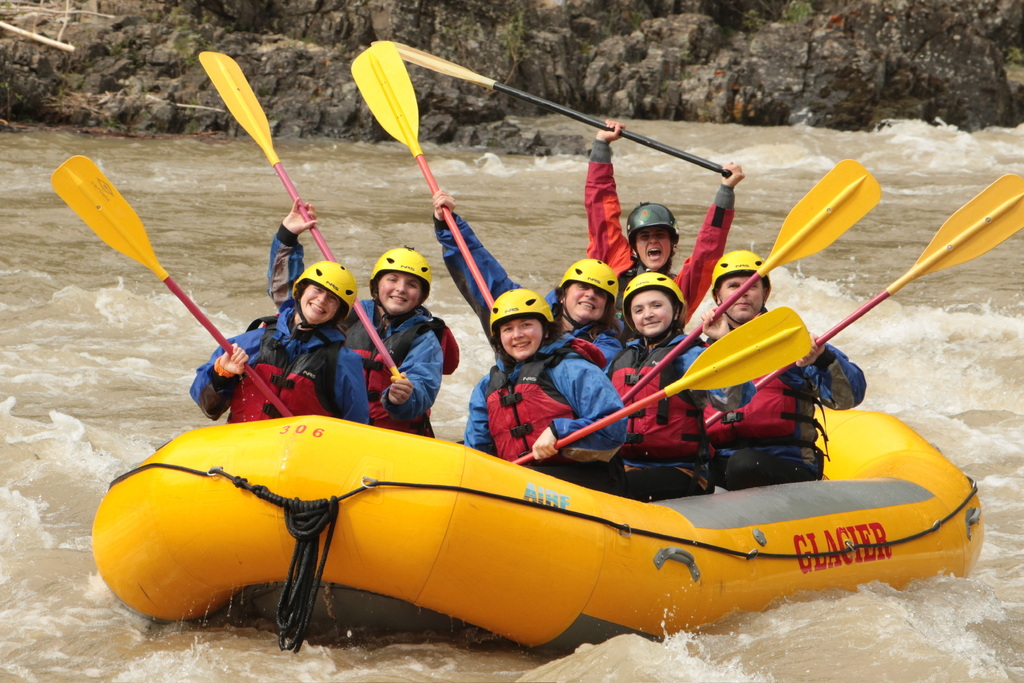 seven people holding oars in the air in a whitewater raft