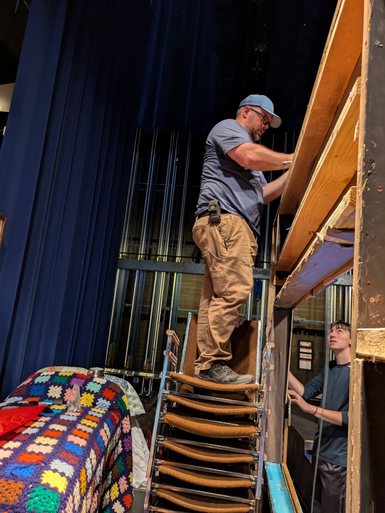Men and youth attaching large house front to fly rail system