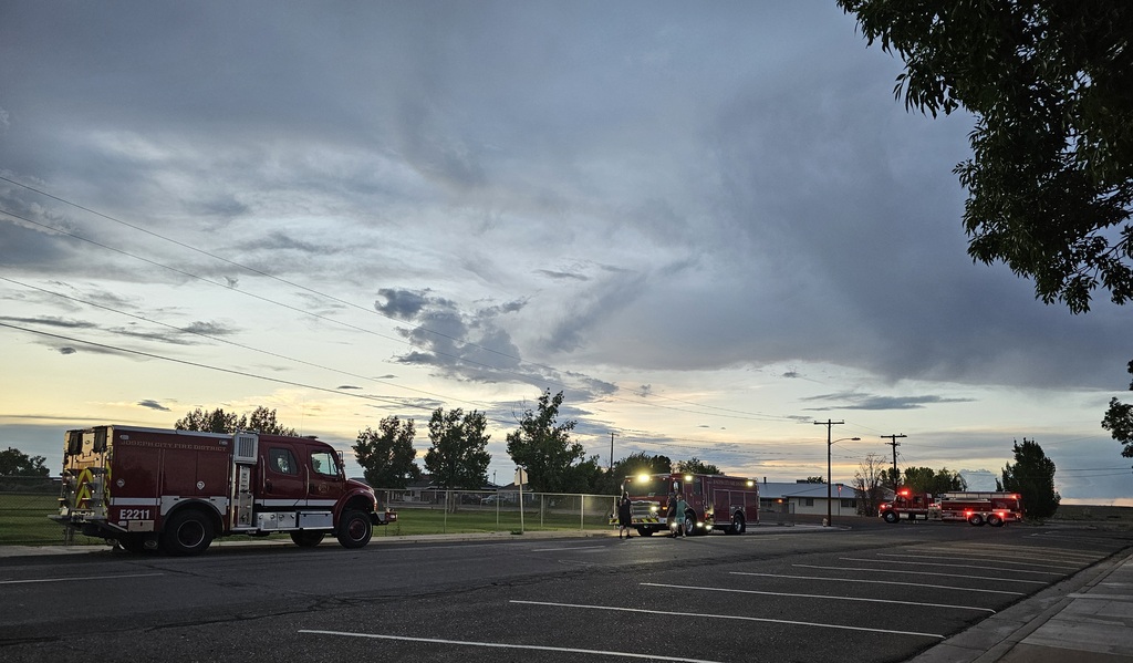 Three fire trucks parked near a school field with a cloudy sky