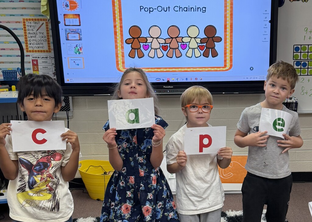 Four first grade students holding large letter cards to spell the word cape.