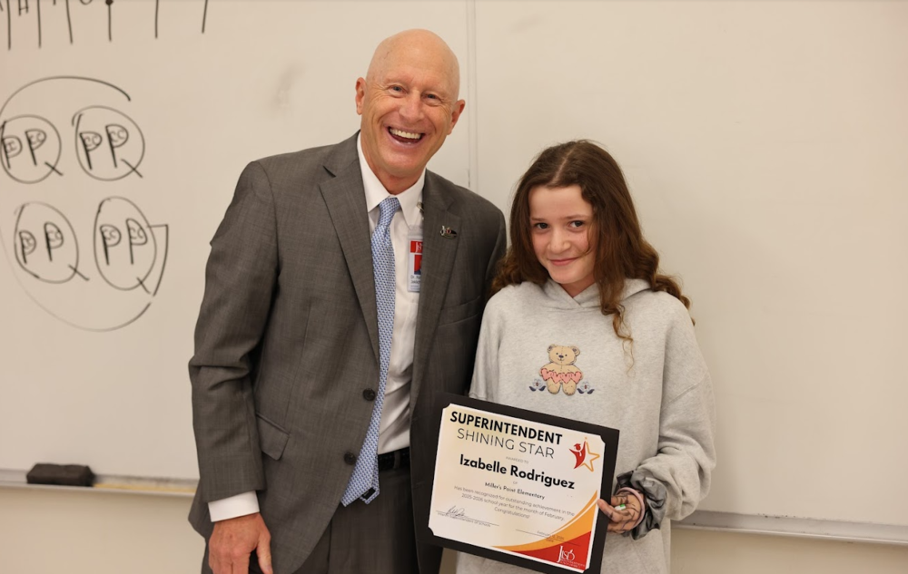 Man and student standing in front of a white board. The student is holding an award.