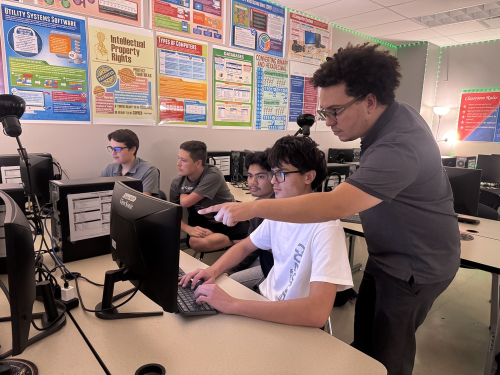 students and teacher looking at a computer.