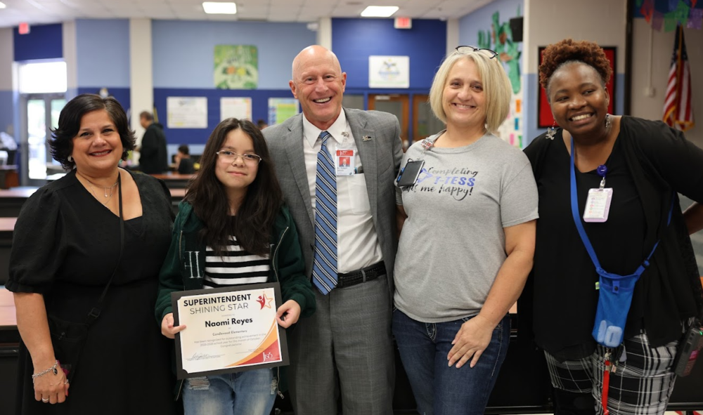 Four adults standing with a student holding an award certificate.