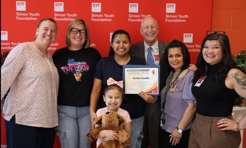 Student holding an award with family and teachers standing in front of Simon Youth Foundation backdrop.