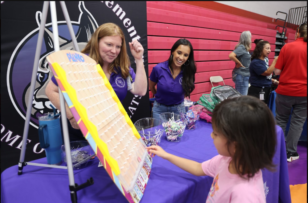 Child playing a game while adults smile at her from behind a table with a purple tablecloth