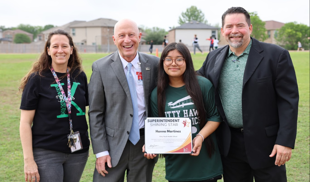 Three  adults standing with a child holding a certificate on the playground.
