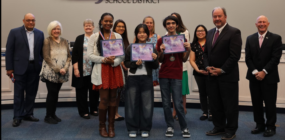 Students standing in front of adults holding certificates.