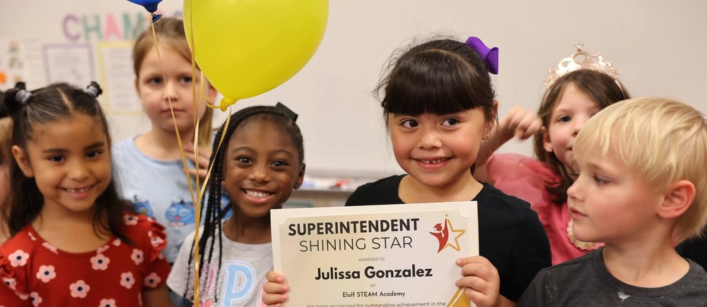 Little girl with a certificate and other students around smiling