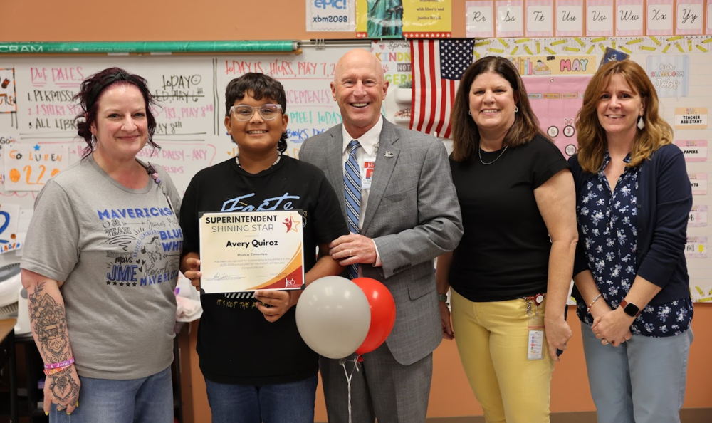Student holding a certificate standing with adults and balloons