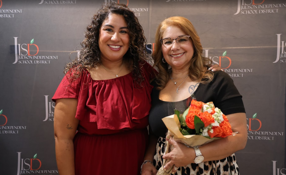 Two women in front of a JISD backdrop , one woman is holding flowers.