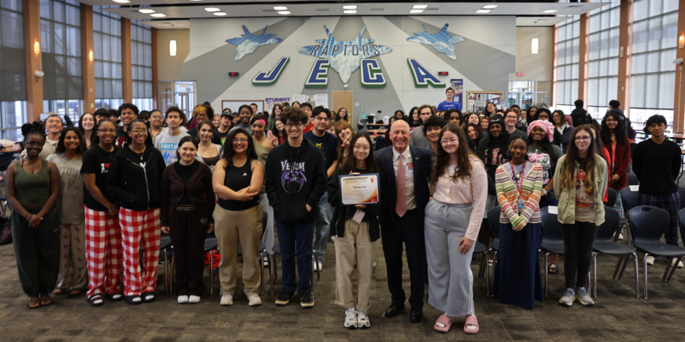 Group of students with a girl in front holding a certificate standing beside a man in a suit.