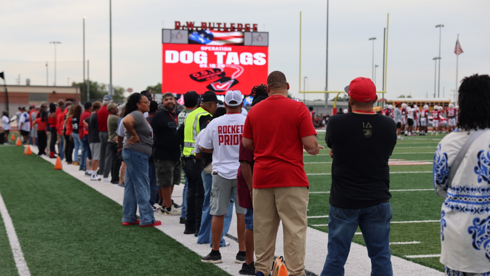 Operation Dog Tags on a jumbotron with people standing on the sideline