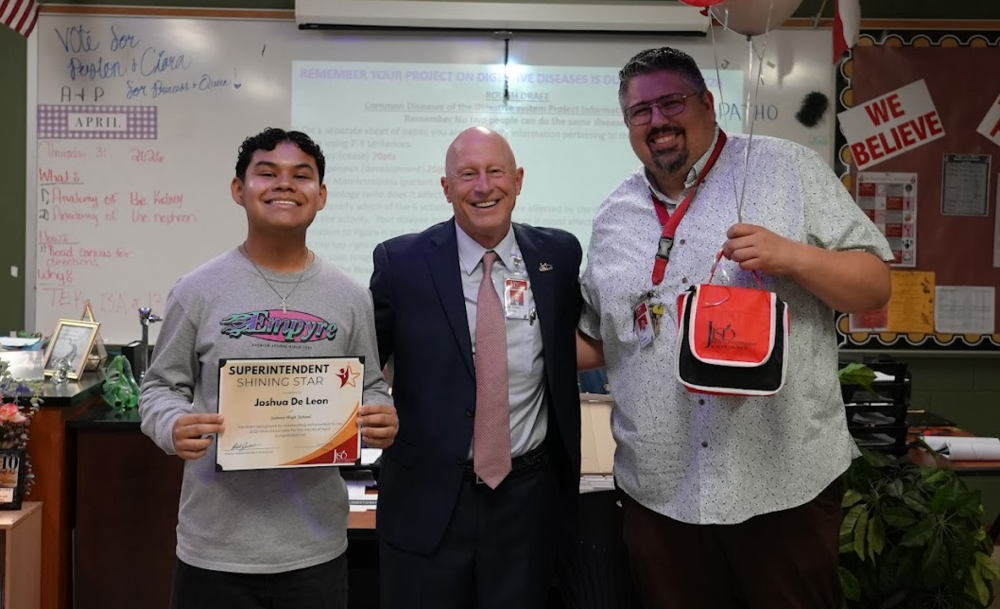 Student holding a certificate standing with 2 men smiling.
