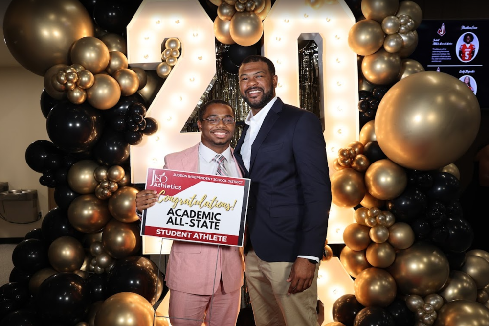 Student holding Academic All State Sign standing in front of balloons with a man.