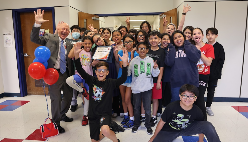 Students and man in suit making funny faces and smiling. One girl is holding an award.