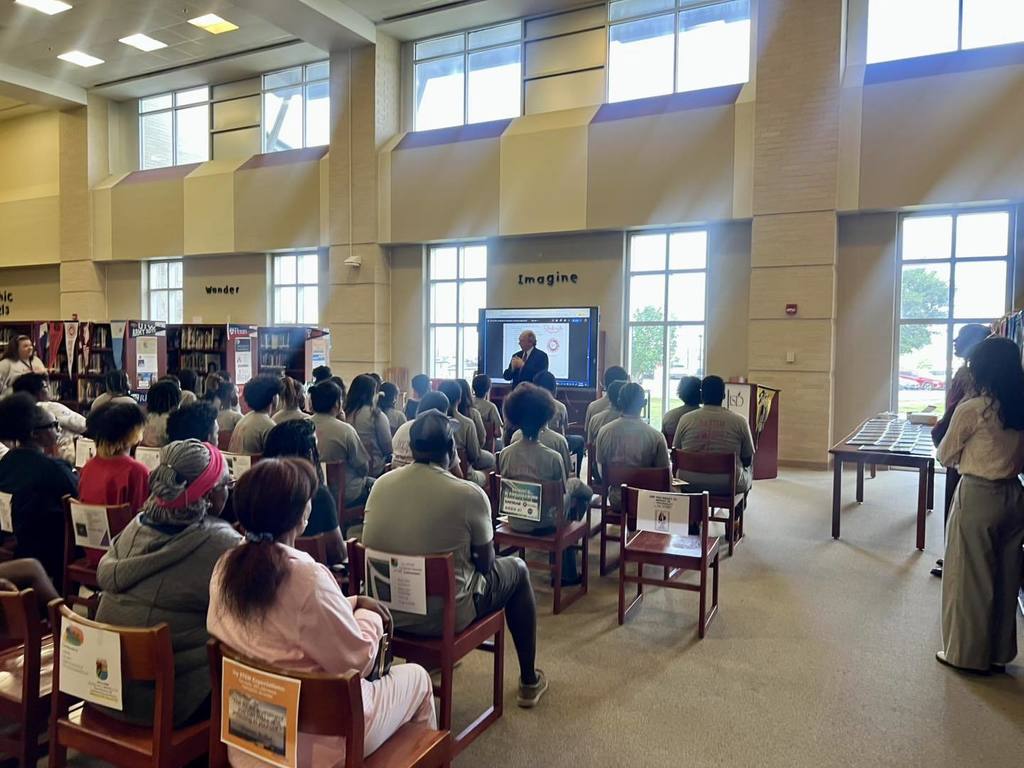 students gathered in a library watching a presentation