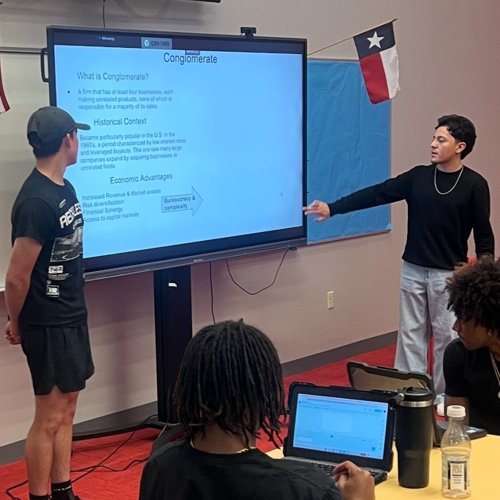 Students at a clear touch panel, presenting to their classmates in the library