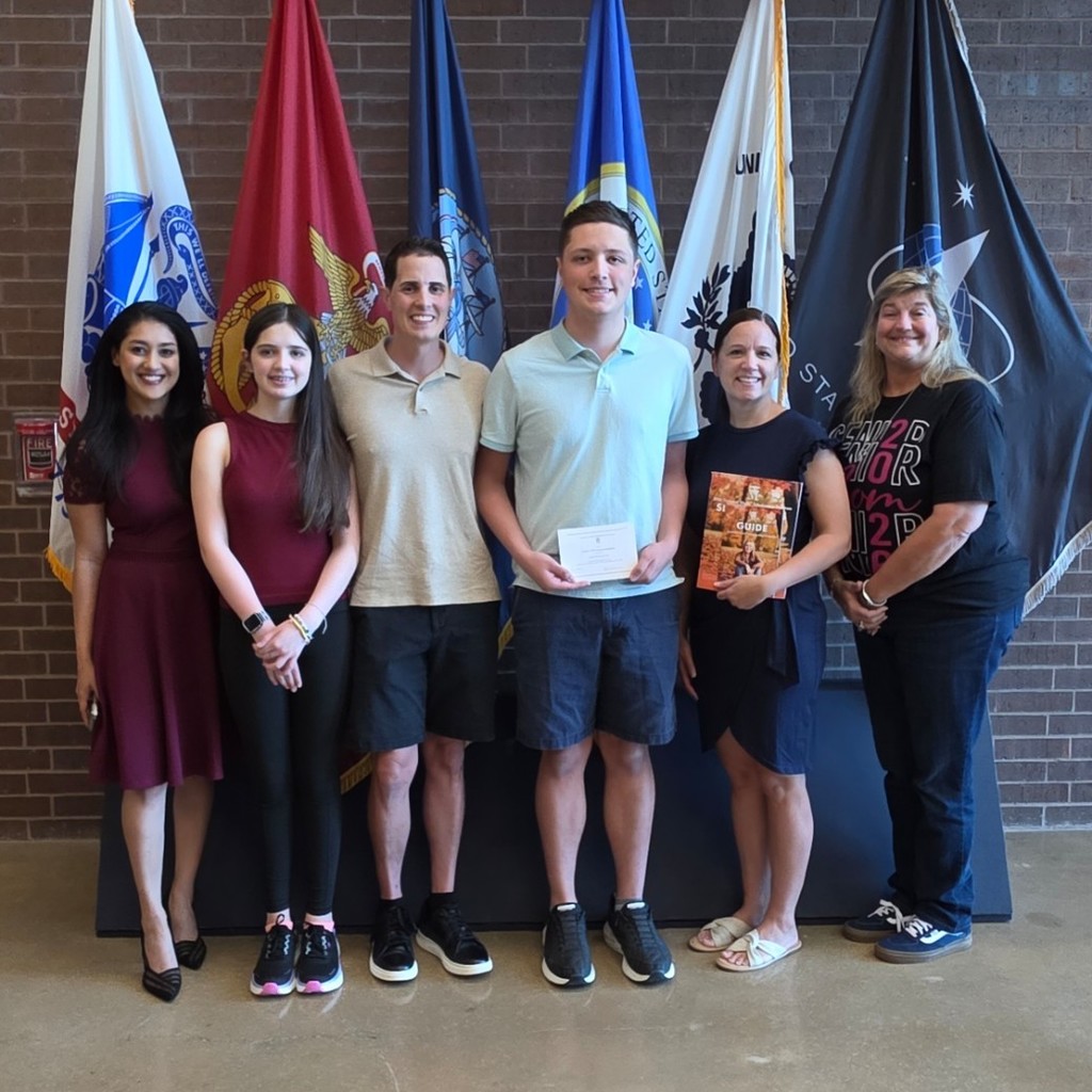 Student, his family, and VMHS principal in front of flags