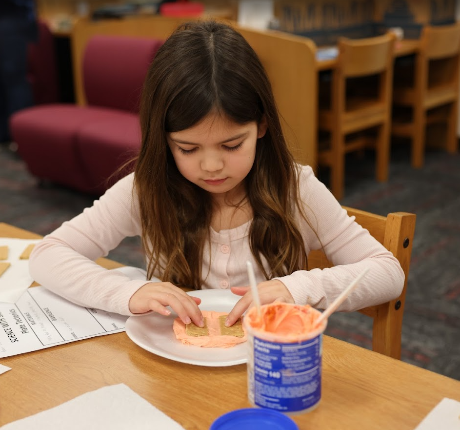 Little girl doing a science experiment with cookies and frosting.