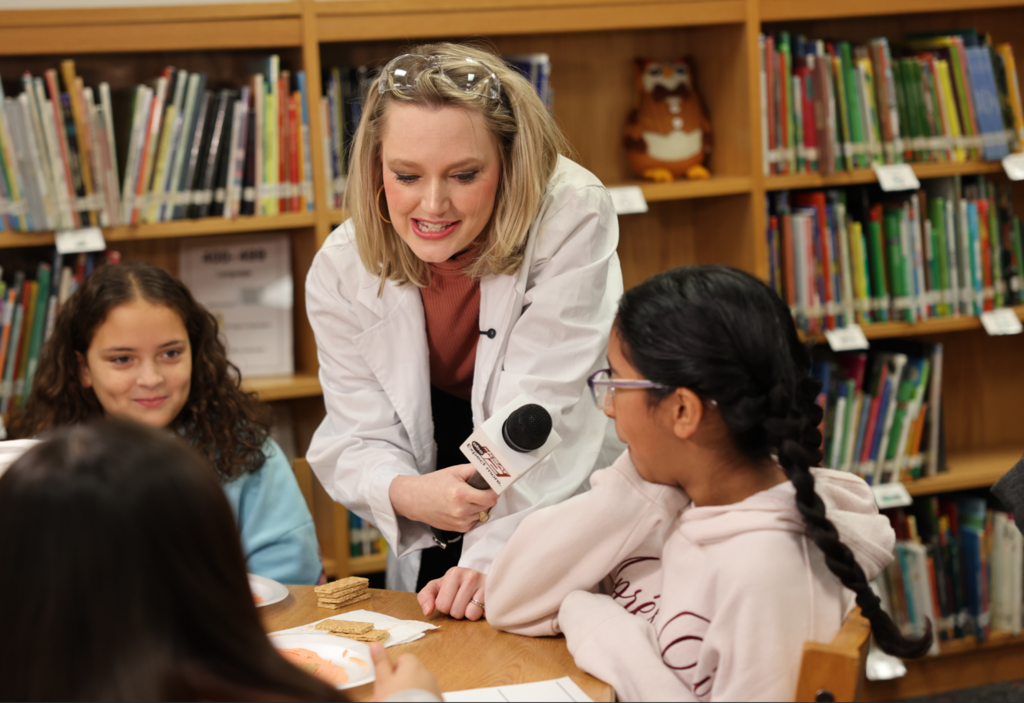 Woman with a microphone with three students at a table.