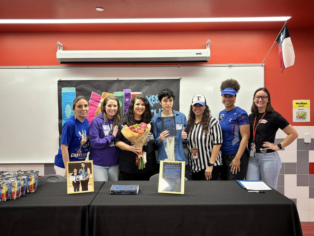 Eleazer with staff and family behind a table with his book showcased. 