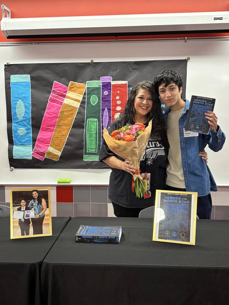 Eleazer posing with his teacher who is also pictured with him in a displayed framed photo on the table next to his book.