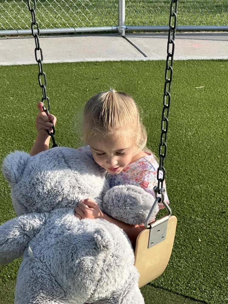 girl swinging with her large gray teddy bear 