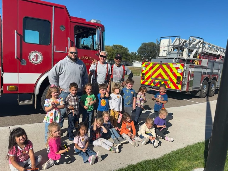 preschool students posing for photo with Firemen in front of fire trucks