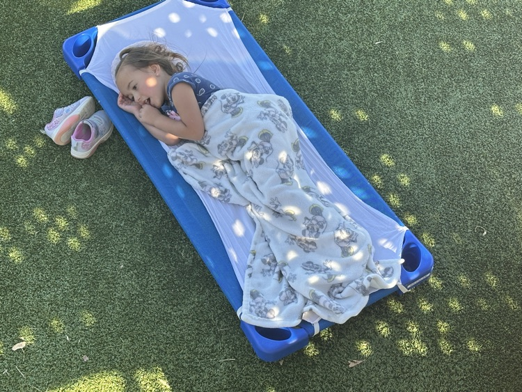 preschool students laying on their mats outside on the playground for nap time 