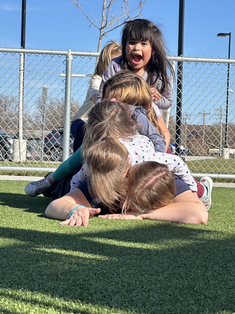 students piling onto the back of teacher laying on the ground with students