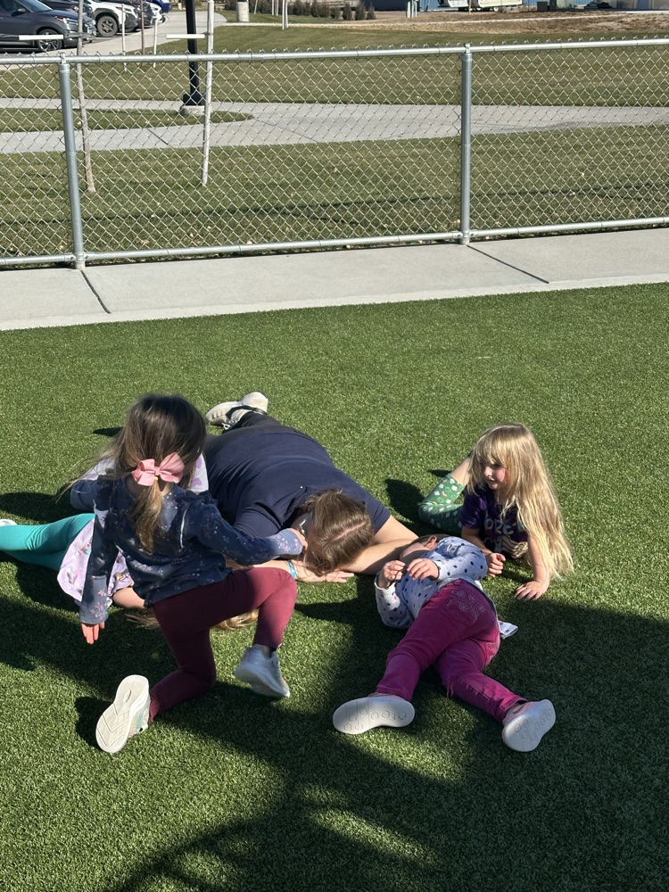 students piling onto the back of teacher laying on the ground with students