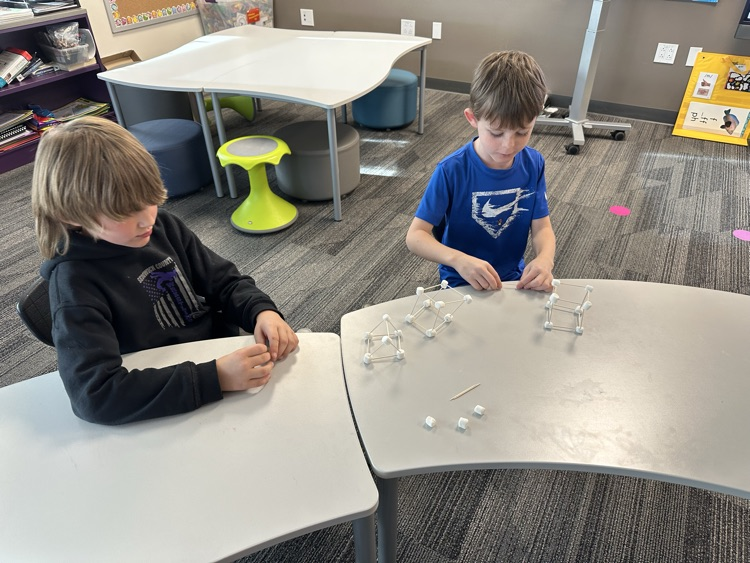 First graders using marshmallows and toothpicks to build 3D shapes in math class.