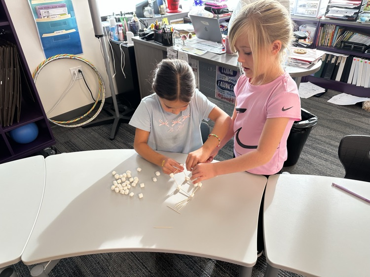 First graders using marshmallows and toothpicks to build 3D shapes in math class.