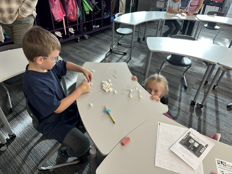 First graders using marshmallows and toothpicks to build 3D shapes in math class.