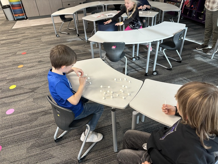 First graders using marshmallows and toothpicks to build 3D shapes in math class.