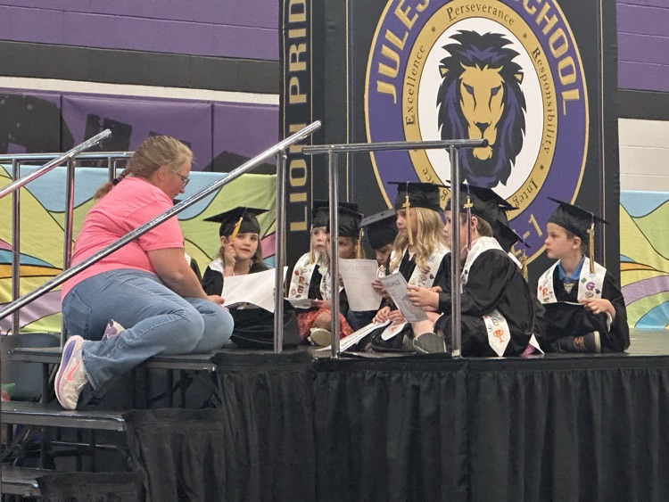 students surrounding teacher sitting on stage