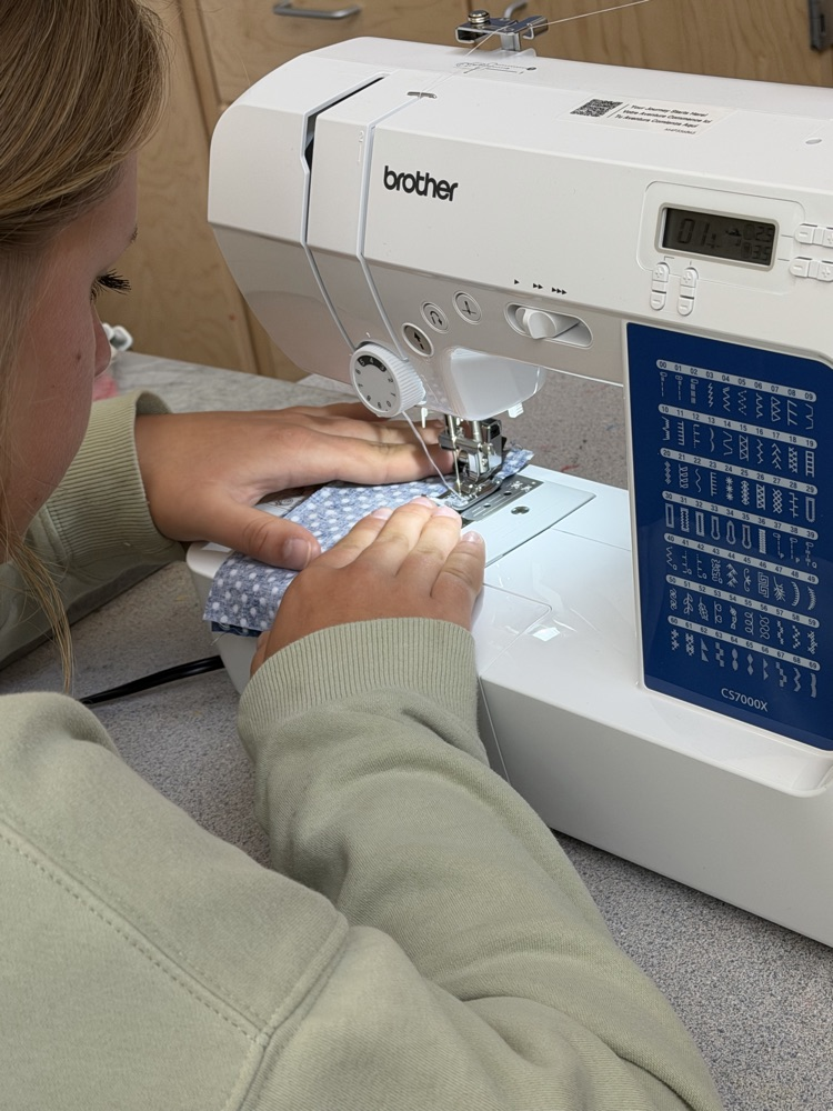 A person using a white Brother sewing machine with a blue screen, sewing a piece of blue fabric.
