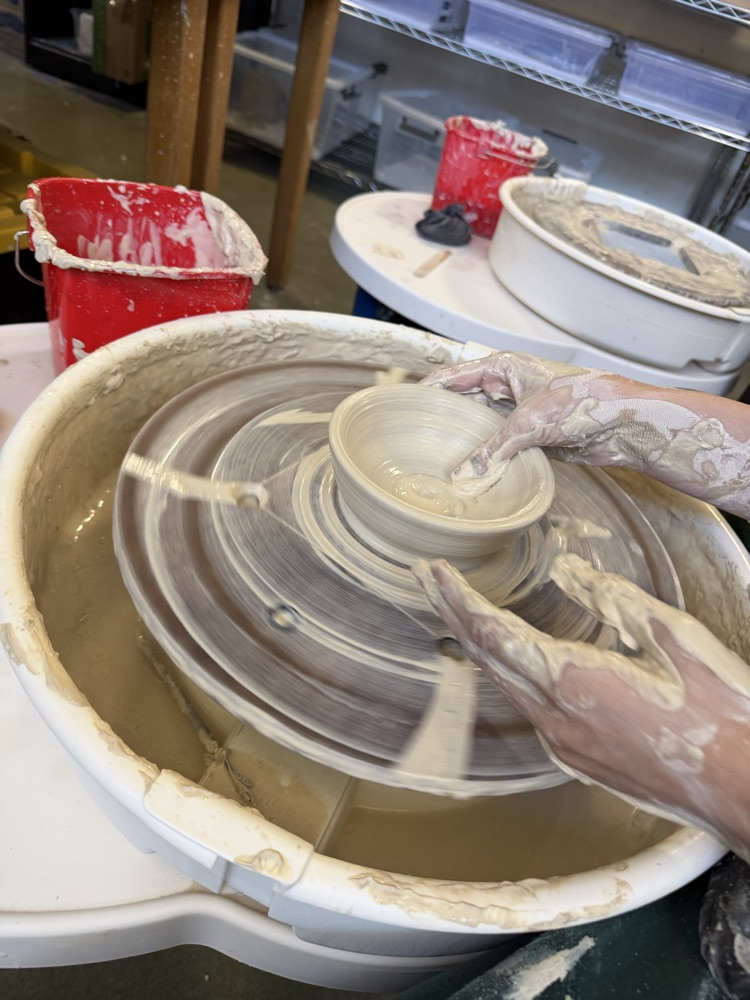 A person is using a pottery wheel with their hands while making a clay bowl.