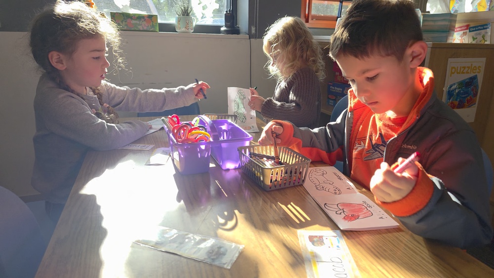 Three young children sitting at a table, they are coloring.