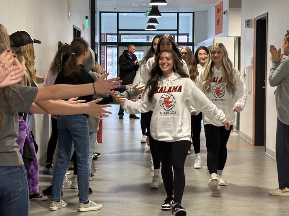 A group of students are walking through a hallway high fiving other students