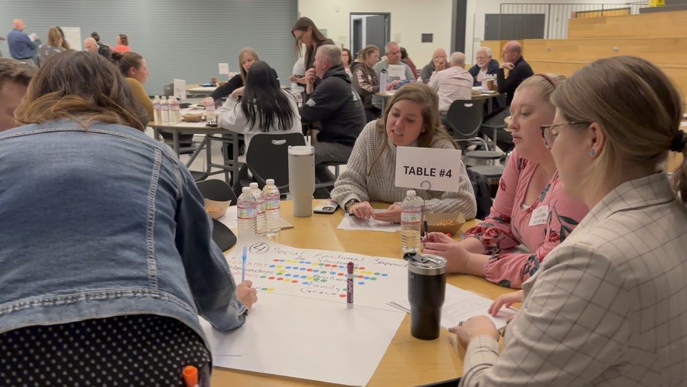 A large group of people sitting around tables, talking and engaging with one another..