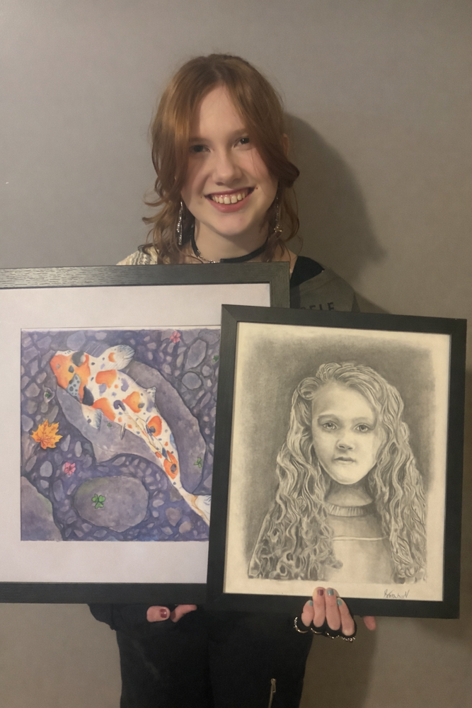 Middle School student holding two framed drawings