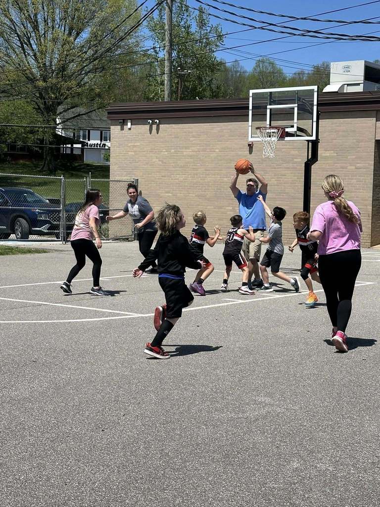 a sissonville elementary staff member grabs a rebound during the game while students try to steal the ball.