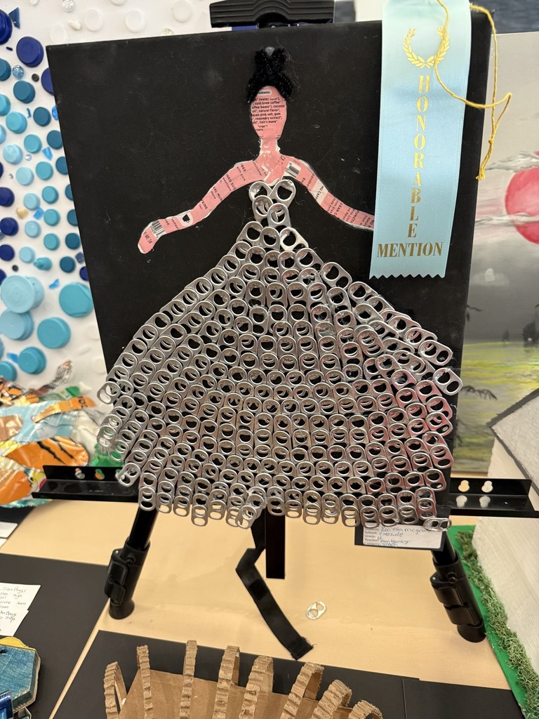 art work that used soda tabs to create a dress for a woman who was made from recycled boxes.