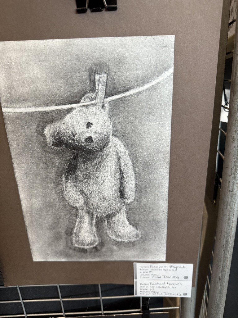 black and white drawing of a teddy bear hanging by his ear on a close line.