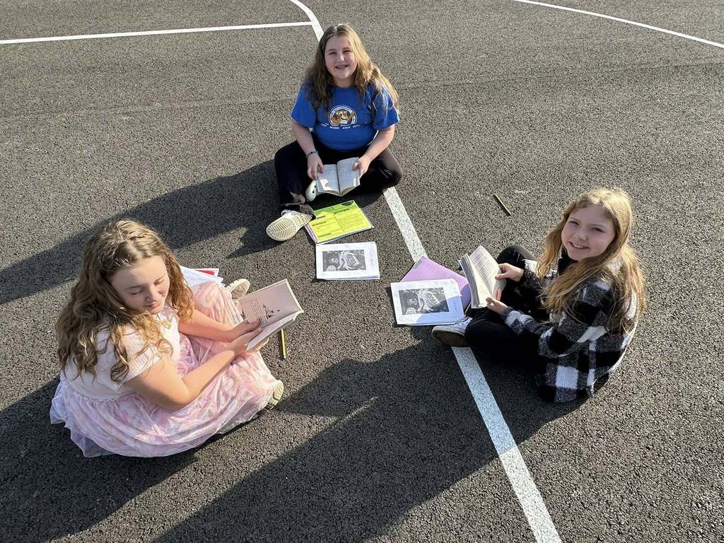 students smiling at the camera while they read a book outside.