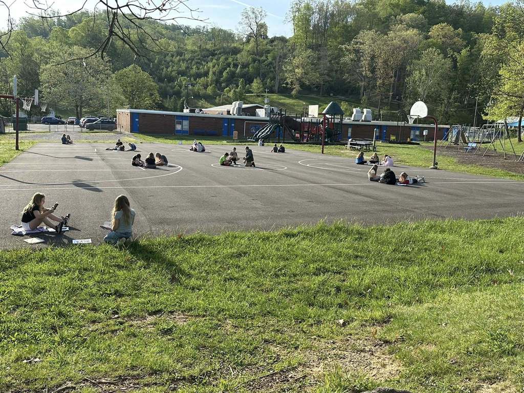 wide shot showing the entire 3rd grade class at alum creek elementary reading on the basketball court on the playground.