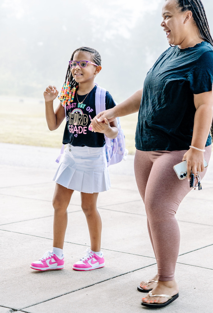 a young girl and her mom saying goodbye as the daughter walks into school. 